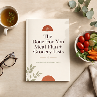 The Done-For-You Meal Plan + Grocery Lists booklet on a pale wood table beside a bowl of fresh vegetables in soft morning light